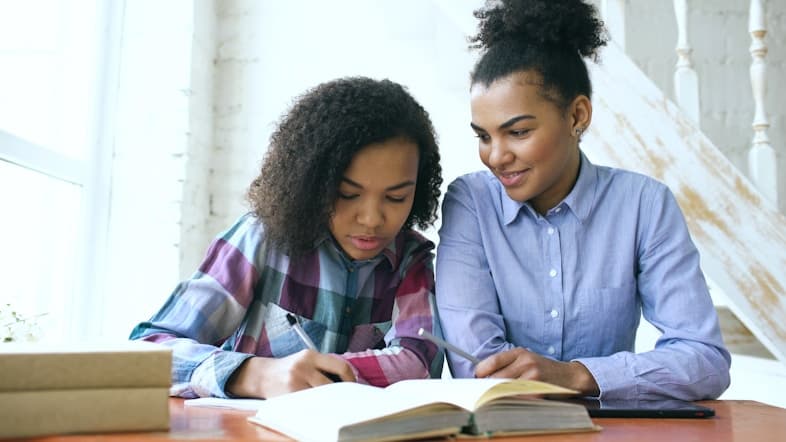 Two students studying together at a desk with open books