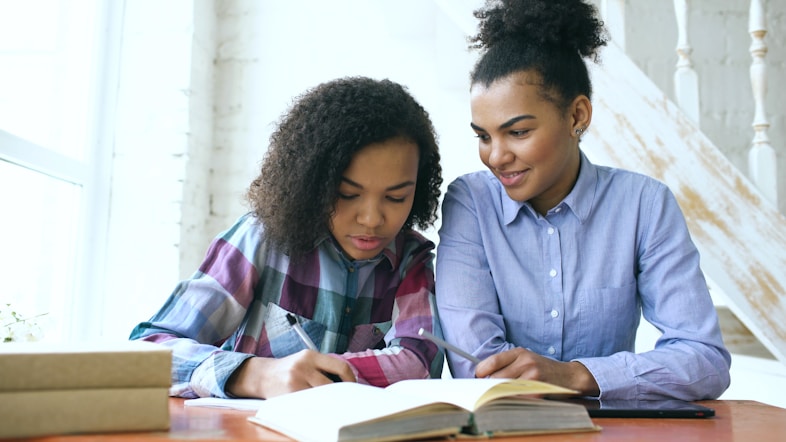 Two students studying together at a desk with open books